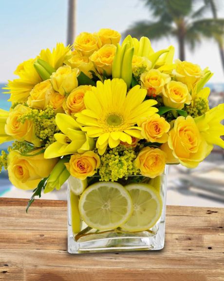 Limonada-Yellow gerbera daisies, yellow roses, yellow tiger lilies, and yellow solidago are designed in a clear glass cube that in decoratively lined with fresh cut lemons and curley willow.-Arrangements