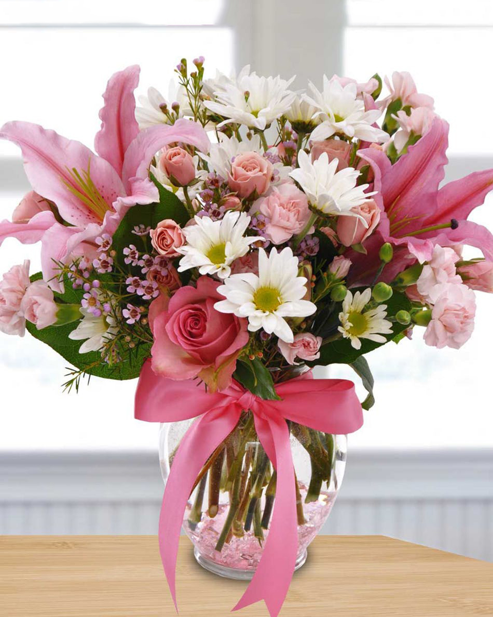 Pink Sonnet Standard 
Pink Sonnet - Pink stargazer lilies, pink mini carnations, pink roses, pink spray roses, white daisy poms, seasonal greens and fillers are elegantly designed in a clear ginger jar vase with a pink bow.

DELIVERY: Every order is hand-delivered direct to the recipient. These items will be delivered by us locally, or a qualified retail local florist.
