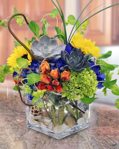 earth and wind-cube arrangement that consists of hydrangea, sunflowers, spray roses, succulents, curley willow, and bear grass. The bottom of the cube is decorated with sea shells and rocks.-cube arrangements