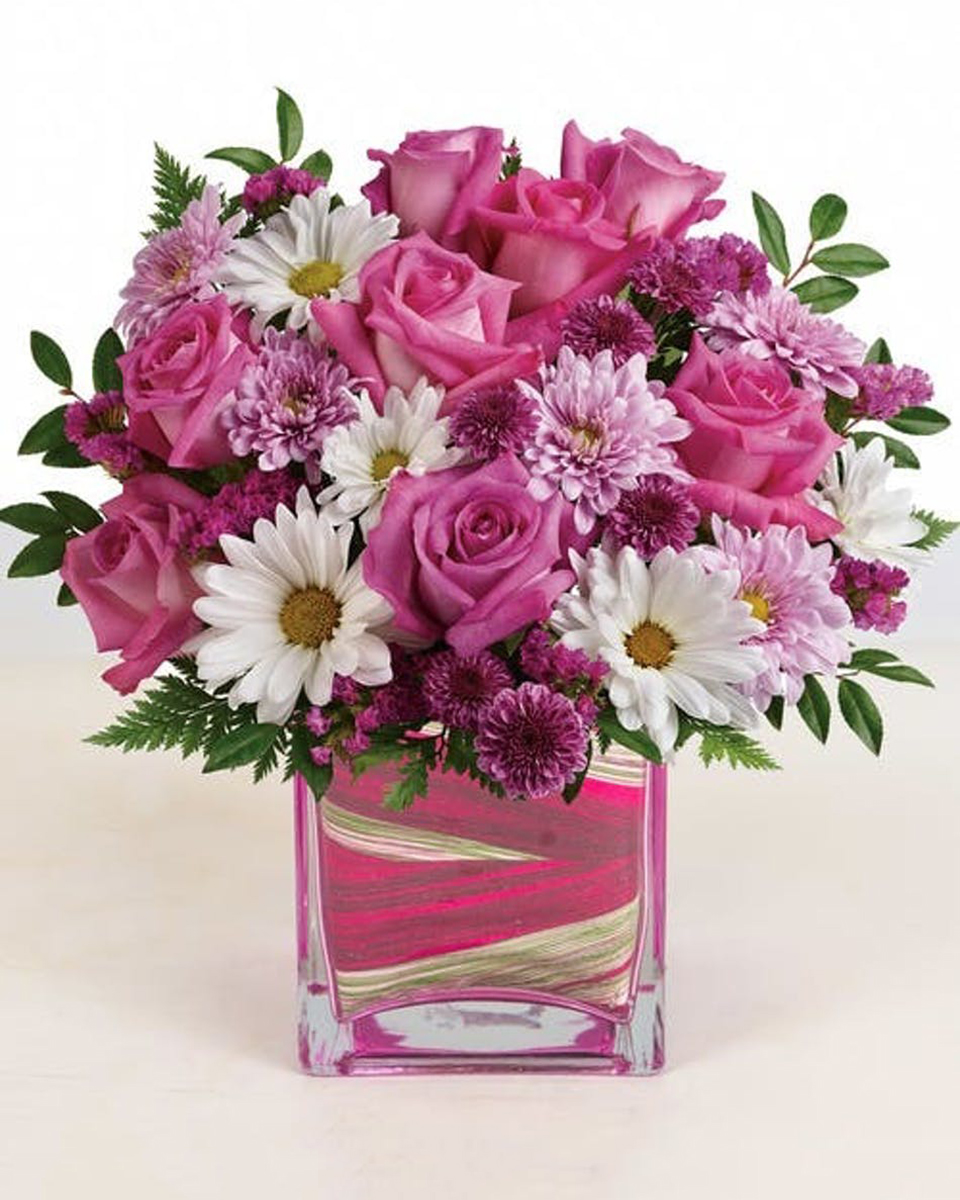 Fashionista Long Beach Premium-in a 7 x 7 Cube This beautiful design features stunning pink roses, purple mums, white daisies and more--it's perfect for any celebration!  Approximate sizes:  Standard 9