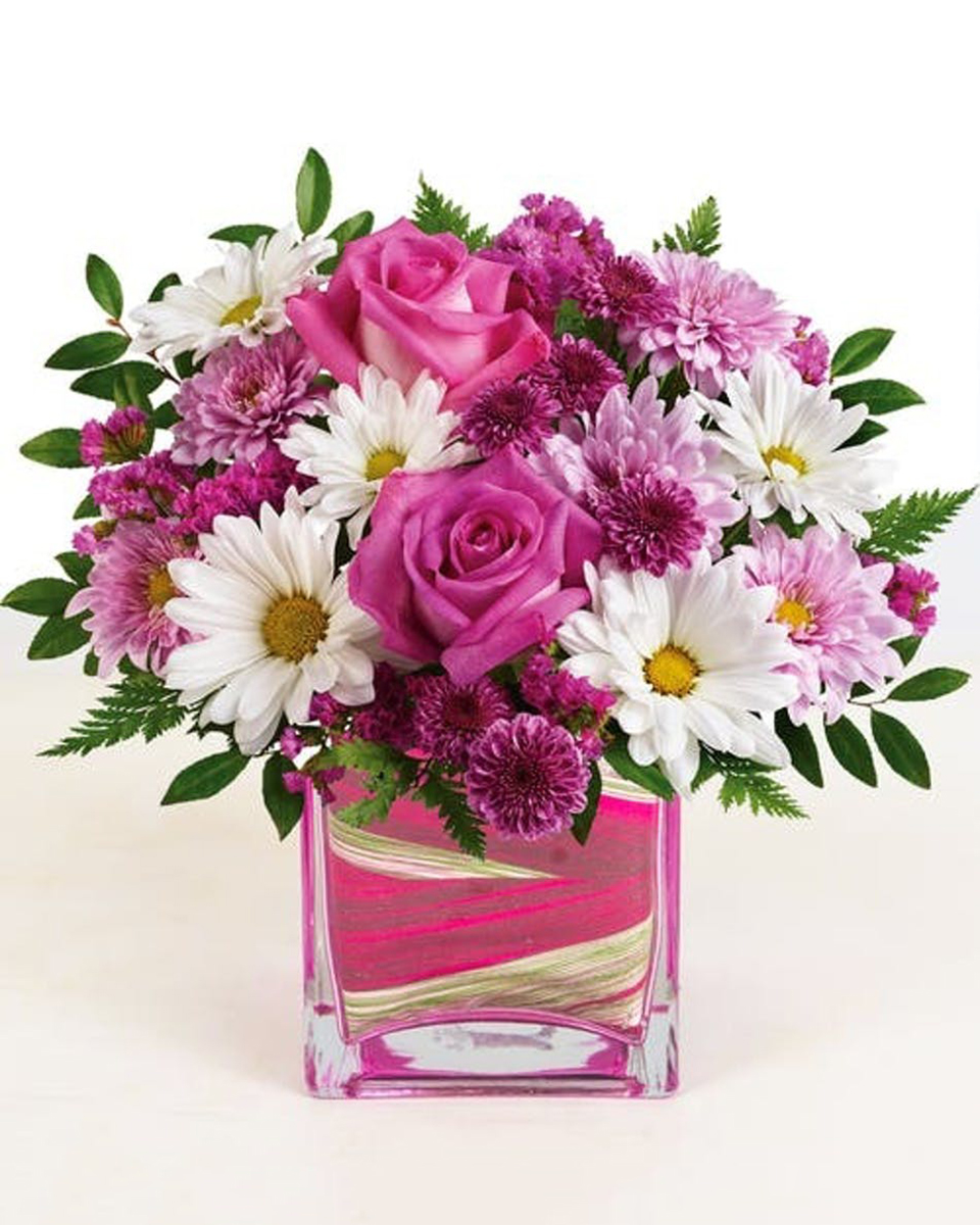 Fashionista Long Beach Standard-in a 5 x 5 Cube This beautiful design features stunning pink roses, purple mums, white daisies and more--it's perfect for any celebration!  Approximate sizes:  Standard 9