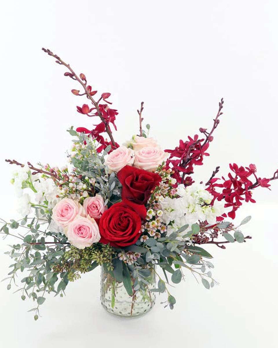 Heart and Soul Standard This best-selling arrangement features red roses, pink spray roses, white stock, unique Red Elephant orchids and loads of seasonal textures presented in a designer glass spin In a clear glass cylinder.