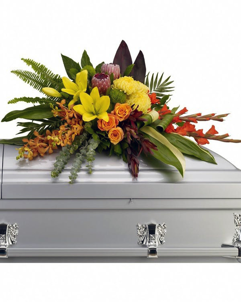 Tropicana Standard Yellow asiatic lilies with orange orchids and roses, red gladioli, pink protea and yellow chrysanthemums are draped across the casket amidst radiating ferns, greens and leaves. Approximately 40